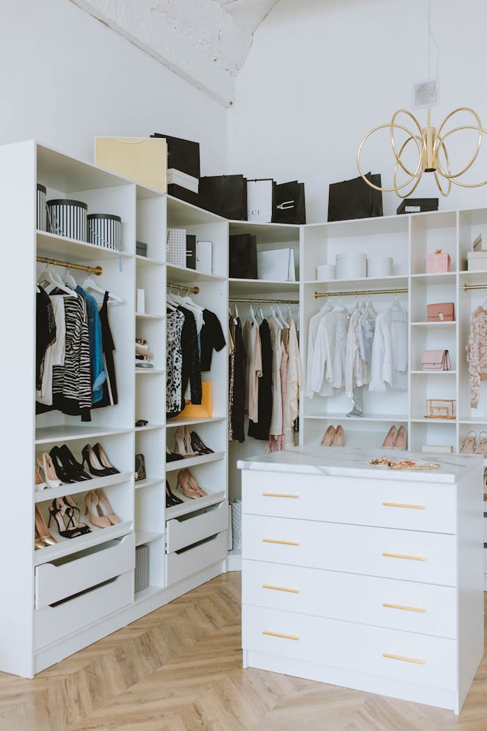 gallery-03 A stylish walk-in closet featuring luxury clothing, shoes, and accessories, with elegant shelving and chandeliers.