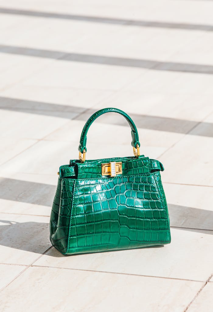 home-img Luxurious green handbag with crocodile texture displayed on a light pavement outdoors in natural daylight.